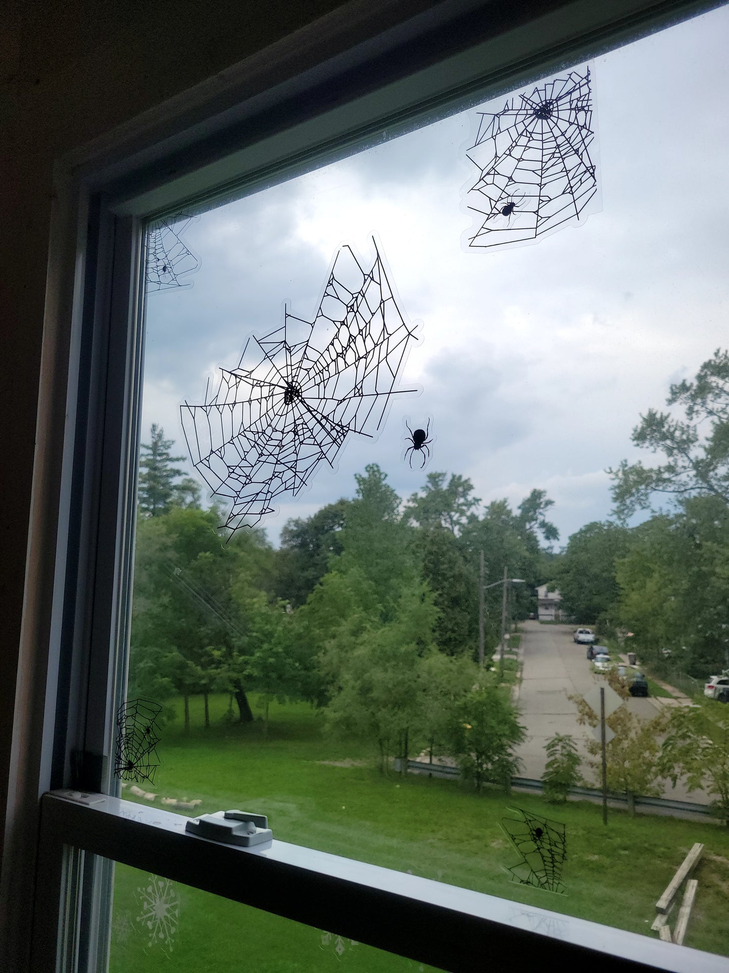 Spider webs static clings for Halloween window decor shown on a window with the sky bright in the background. Black ink on clear material contrasts sharply when backlit