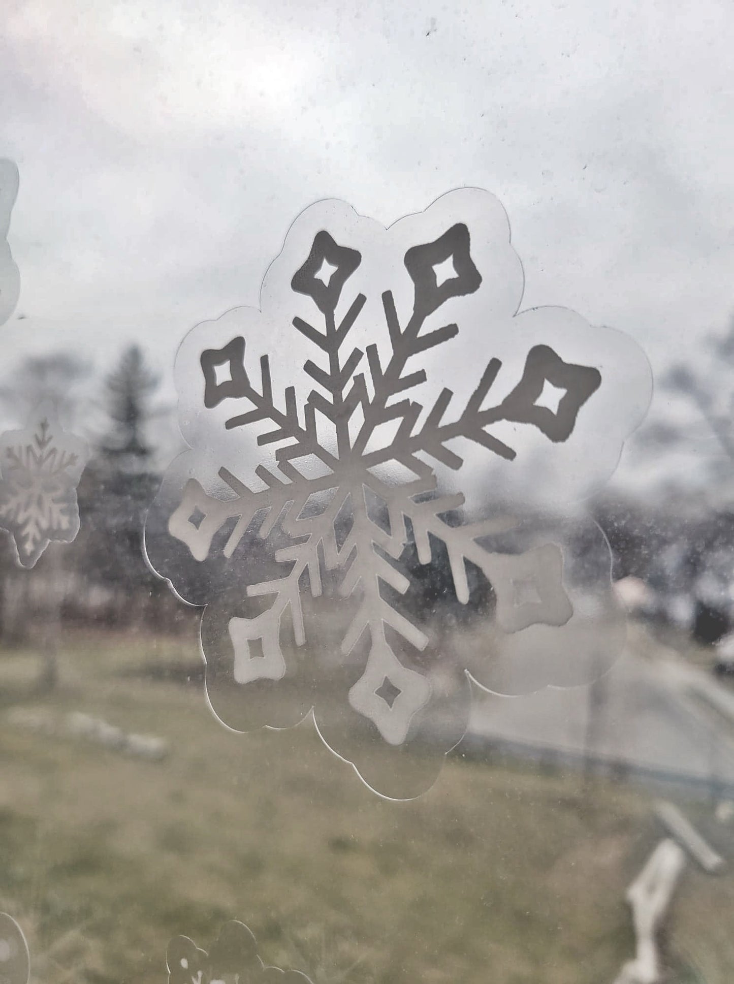 A closeup photo of one of the snowflakes that come in the static cling snowflake set by InkBird Print Studio. Crisp white ink on a clear contour cut static cling piece.