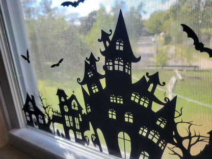 A closeup shot of part of our Our Spooky Town Halloween static cling window decoration. Black ink on a clear material, applied to a window with a sunny exterior seen in the background.