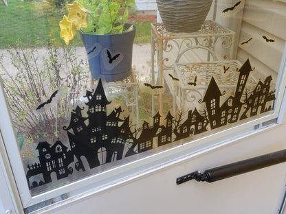 A photo of our Our Spooky Town Halloween static cling window decoration applied to a storm door. Black ink on a clear material, applied to a window with a sunny exterior seen in the background.